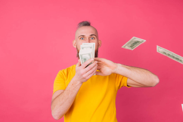 European man on pink red background with fan on 100 dollars happy excited throwing in air isolated space - Zdjęcie, obraz