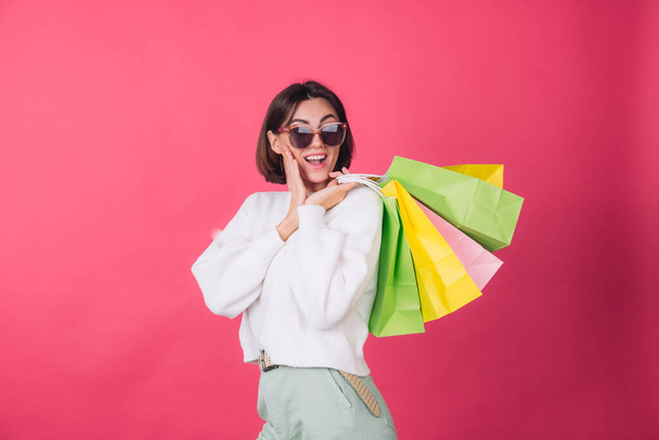 Woman in casual white sweater and sunglasses on pink red background holding shopping bags shocked amazed excited  isolated copy space - Fotografie, Obrázek