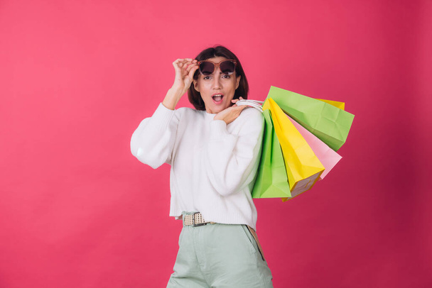Woman in casual white sweater and sunglasses on pink red background holding shopping bags shocked amazed excited  isolated copy space - Φωτογραφία, εικόνα