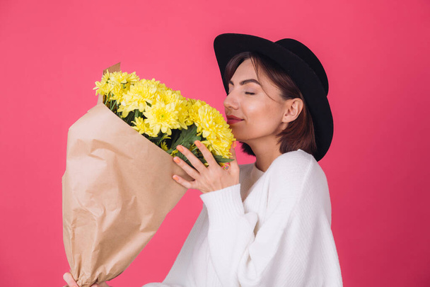 Stilvolle Frau mit Hut auf rosa rotem Hintergrund riecht großen Strauß gelber Blumen, Frühlingsstimmung, glückliche Emotionen isolierten Raum mit geschlossenen Augen - Foto, Bild