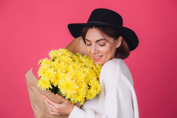 Стильна жінка в капелюсі на рожево-червоному тлі посмішка тримає великий букет жовтих квітів, весняний настрій, щасливі емоції ізольовані простір
  - Фото, зображення
