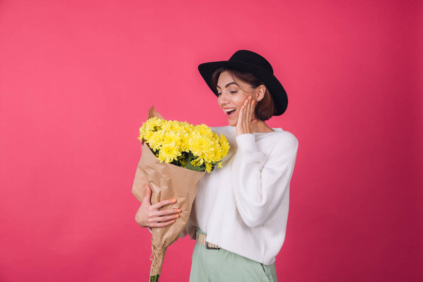 Stylish woman in hat and casual white sweater on pink red background smile hold large bouquet of yellow flowers, spring mood, isolated space amazed excited surprised - Photo, Image