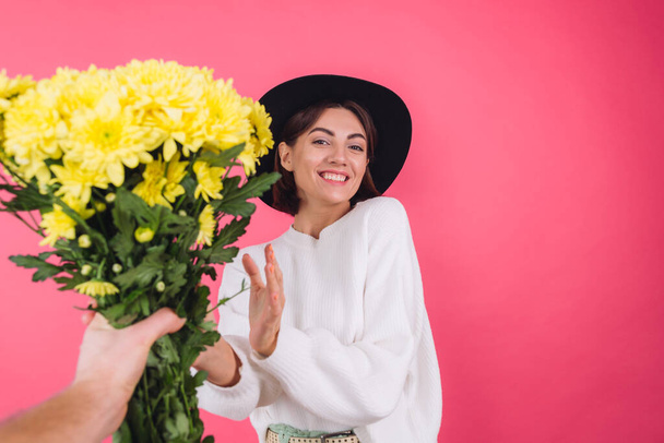 Stylish woman in hat and casual white sweater on pink red background gets large bouquet of yellow flowers, spring mood, isolated space amazed excited surprised - Zdjęcie, obraz