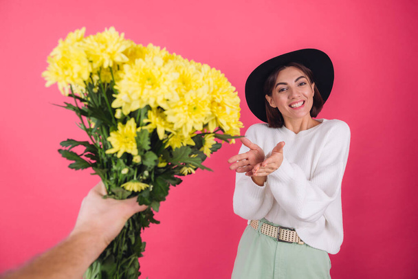 Şapkalı şık bir kadın ve pembe arka planda sıradan beyaz bir kazak büyük bir buket sarı çiçek alır, bahar havası, izole edilmiş bir yer şaşırır. - Fotoğraf, Görsel