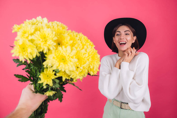 Mujer con estilo en sombrero y suéter blanco casual sobre fondo rojo rosado obtiene un gran ramo de flores amarillas, humor de primavera, espacio aislado sorprendido emocionado sorprendido - Foto, imagen