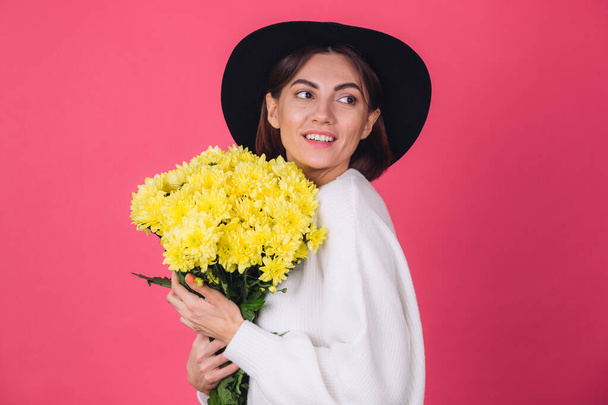 Stilvolle Frau mit Hut und lässigem weißen Pullover auf rosa rotem Hintergrund halten Strauß gelber Blumen, Frühlingsstimmung, isolierter Raum glückliches Lächeln - Foto, Bild
