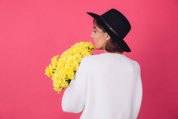 Stílusos nő kalapban és alkalmi fehér pulóver rózsaszín piros háttér hold csokor sárga virágok, tavaszi hangulat, elszigetelt tér vissza nézet - Fotó, kép