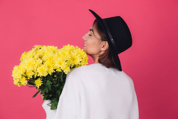 帽子のスタイリッシュな女性とピンクの赤い背景のカジュアルな白いセーター黄色の花の花束を保持し、春の気分、隔離されたスペースバックビュー - 写真・画像