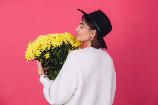 Stylish woman in hat and casual white sweater on pink red background hold bouquet of yellow flowers, spring mood, isolated space back view - Photo, Image
