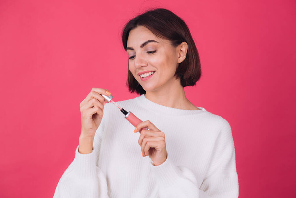 Stylish woman in casual white sweater on pink red background isolated space happy positive hold lipstick - Foto, Imagem