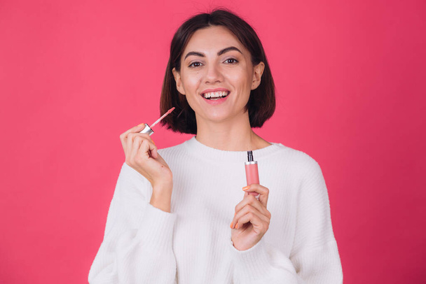 Stylish woman in casual white sweater on pink red background isolated space happy positive hold lipstick - 写真・画像