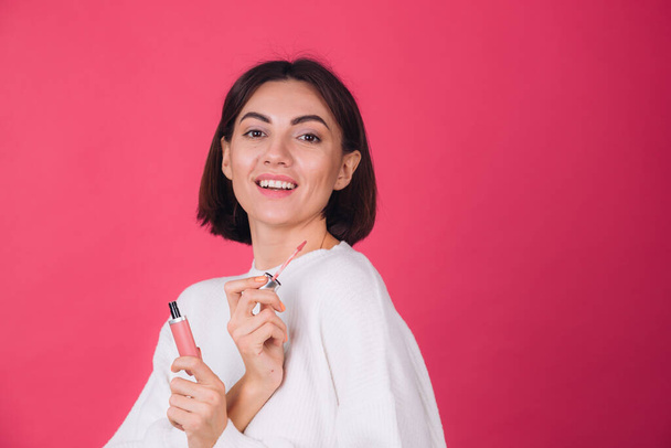 Stylish woman in casual white sweater on pink red background isolated space happy positive hold lipstick - Fotografie, Obrázek