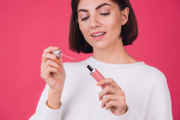 Stylish woman in casual white sweater on pink red background isolated space happy positive hold lipstick - Foto, imagen