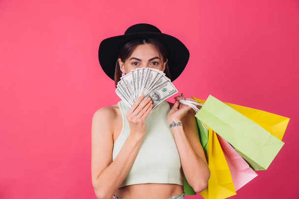 Stylish woman in hat on pink red background isolated space smile  excited hold fan of 100 dollars money and shopping bags, excited surprised  cover face - Photo, Image