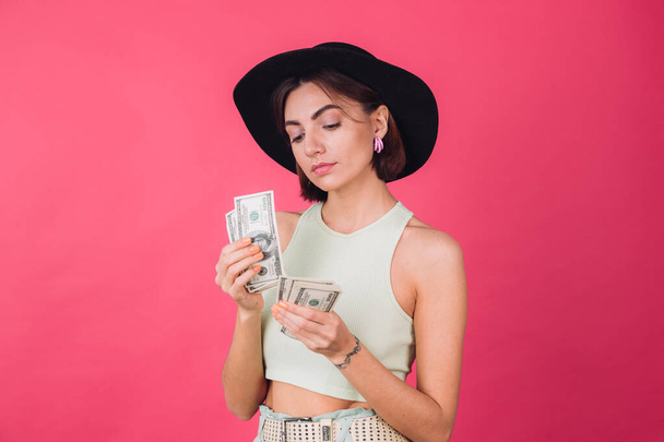 Stylish woman in hat on pink red background isolated space smile  excited hold fan of 100 dollars money thoughtful count money - 写真・画像