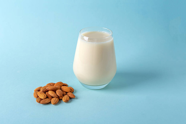 Glass of organic vegan dairy free milk from almonds nuts. Healthy breakfast with vegetarian alternative drink on blue background. Copy space for text - Photo, Image