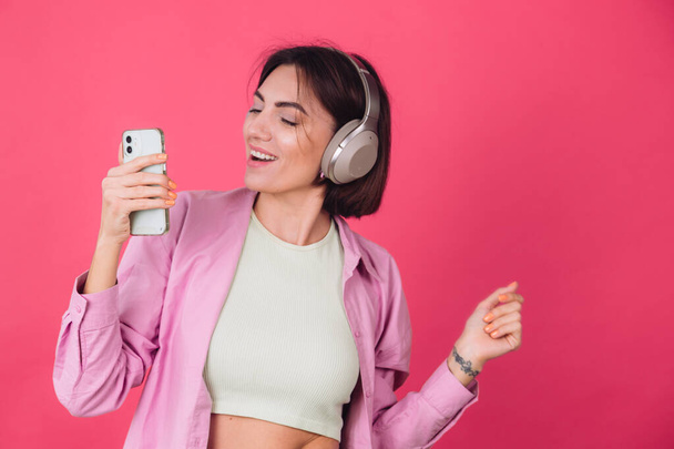Ευτυχισμένη θετική γυναίκα σε ακουστικά σε ροζ κόκκινο φόντο θετικό χορό κινείται απολαμβάνοντας τον ήχο - Φωτογραφία, εικόνα
