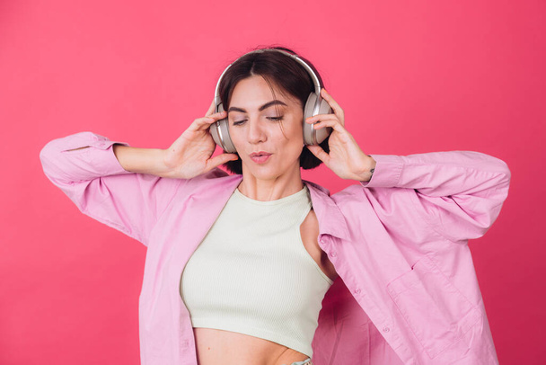 Mujer positiva feliz en auriculares sobre fondo rojo rosa bailando positiva en movimiento disfrutando del sonido - Foto, Imagen