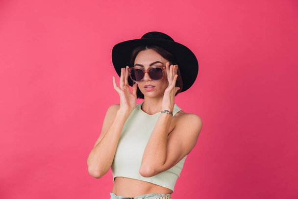 Beautiful stylish woman in hat and sunglasses posing over pink red background, isolated copy space - Φωτογραφία, εικόνα