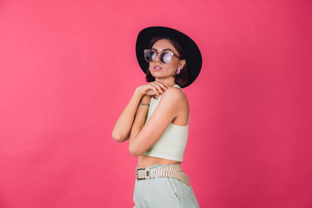 Beautiful stylish woman in hat and sunglasses posing over pink red background, isolated copy space - 写真・画像