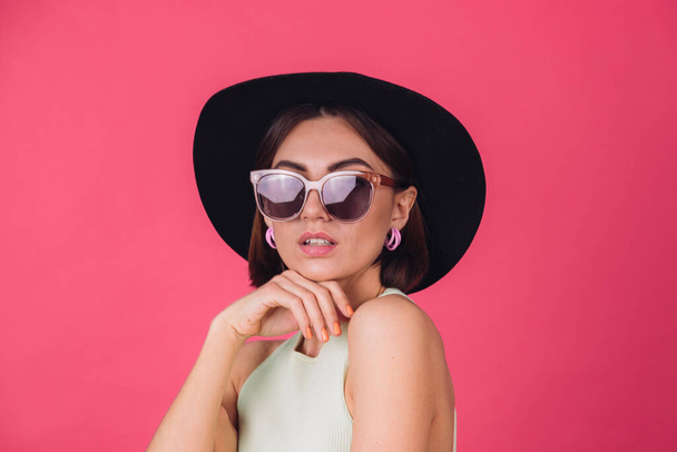 Hermosa mujer elegante en sombrero y gafas de sol posando sobre fondo rojo rosa, espacio de copia aislado - Foto, Imagen