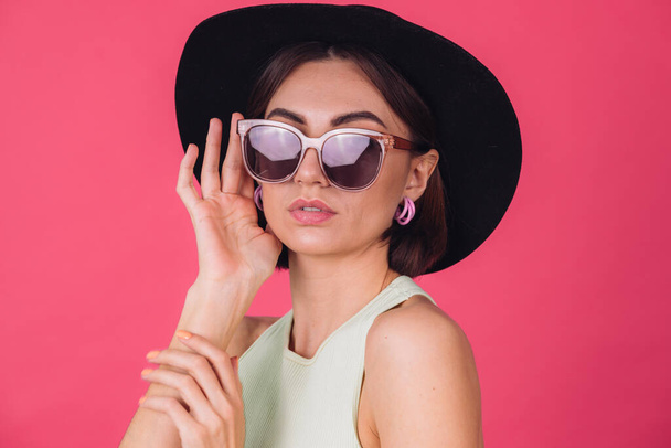 Beautiful stylish woman in hat and sunglasses posing over pink red background, isolated copy space - Photo, Image