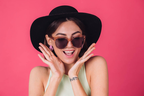 Hermosa mujer con estilo en sombrero y gafas de sol posando sobre fondo rojo rosa feliz emociones emocionadas asombradas, espacio de copia aislado - Foto, imagen