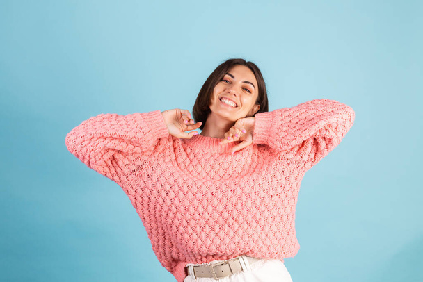 Junge Brünette in warmem rosa Pullover isoliert auf blauem Hintergrund glücklich positiver Tanz bewegt - Foto, Bild