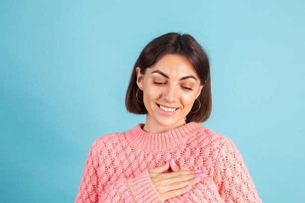 Giovane bruna in caldo maglione rosa isolato su sfondo blu che tiene le mani piegate sul petto, spazio copia del cuore - Foto, immagini