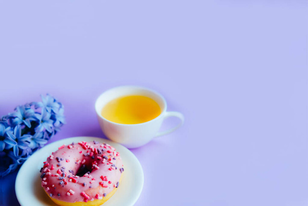 Rosado azúcar esmaltado donut, taza de té y flor de jacinto sobre fondo colorido. - Foto, imagen