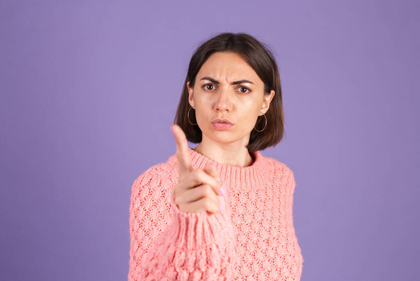 Young brunette in sweater isolated on purple background shouts angrily, reproachfully accuses you, points directly to camera, blames you - Photo, Image