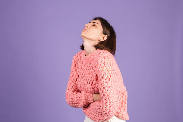 Junge Brünette in rosa Pullover isoliert auf lila Hintergrund leiden Bauchschmerzen mit schmerzhafter Fratze, Gefühl plötzlicher Periodenkrämpfe, Gynäkologie-Konzept - Foto, Bild
