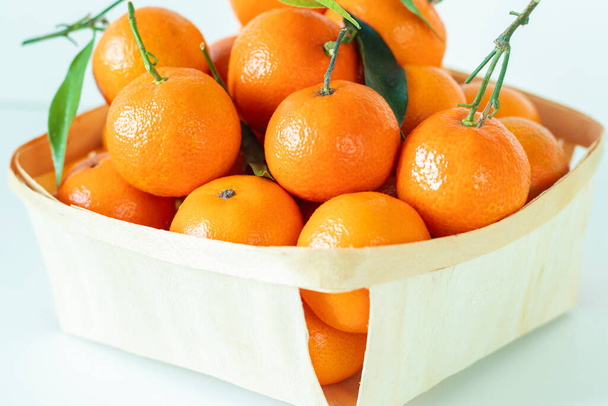 Fresh tangerines with leaves, stands close to a wood basket with white background. Close-up. Selective focus. - Photo, Image
