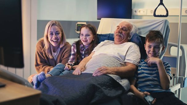 Patient âgé et visiteurs regardant la télévision ensemble - Photo, image