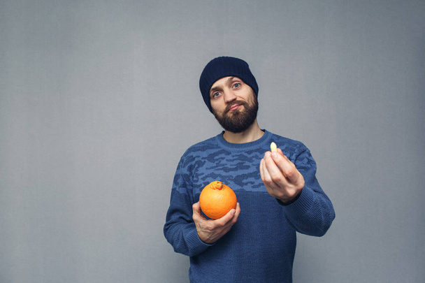 Brodaty facet trzyma w rękach pomarańczę i czopek na hemoroidy. Koncepcja hemoroidów - Zdjęcie, obraz