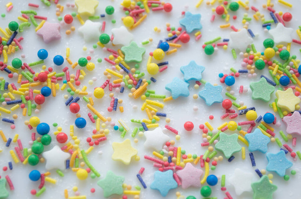 Multi-color festive background of a scattering of sugar candy sprinkles for cupcakes and other pastries in form of stars, sticks and balls. Pastel colors of red, pink and green, blue and yellow. - Фото, изображение