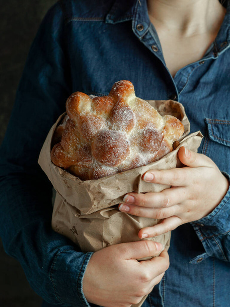 Traditional mexican bread of the dead "pan de muerto" in the young womans hands, blue background - Photo, Image