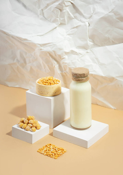 Vegetable pea milk in a bottle and chickpeas in bowl on white podium,pedestal on beige crumpled paper background. shadows. lactose free vegan product.Modern composition.Isometric diagonal projection - Photo, Image