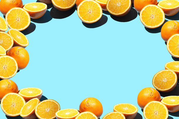 Hele sinaasappels en helften in hard licht op een blauwe naadloze achtergrond gerangschikt aan de rechterkant het creëren van een frame, een template - Foto, afbeelding