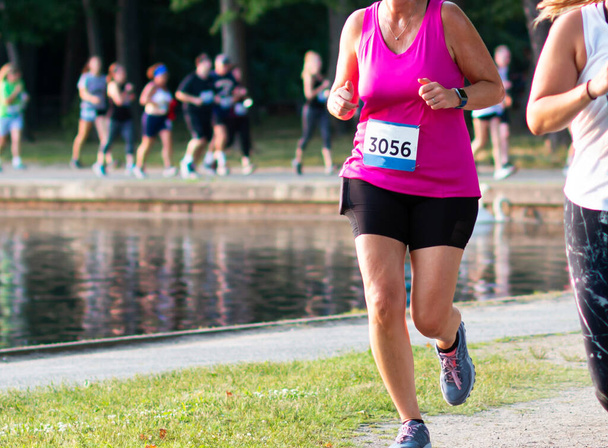 Corredor en foco con corredores borrosos en el fondo corriendo alrededor de Belmont Lake durante una carrera de 5K. - Foto, imagen