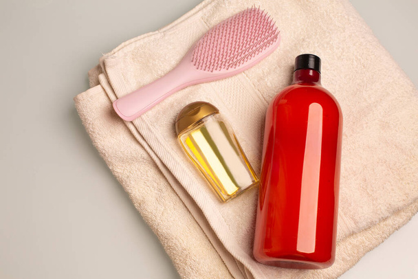 Kit de xampu, óleo de cabelo de tratamento e pente deitado em uma toalha de banho em um banheiro. Espaço para texto - Foto, Imagem
