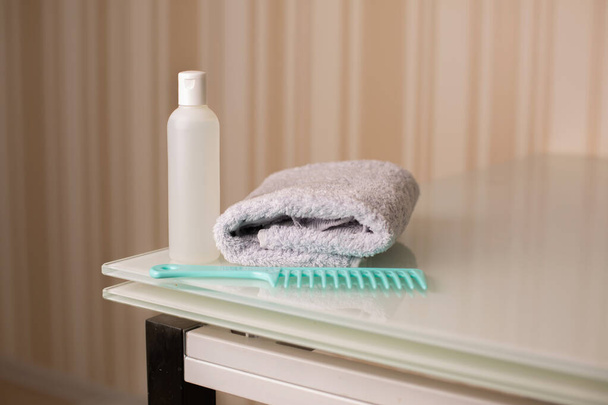 Botella de champú natural y peine con toalla de baño sobre un escritorio sobre un fondo beige neutro. Espacio para texto - Foto, imagen