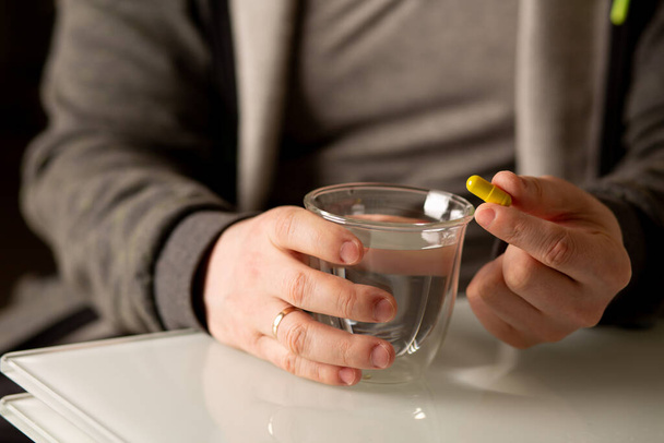 Man holding multivitamin capsule and glass of water. Closeup shot - Photo, image