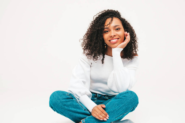 Beautiful black woman with afro curls hairstyle.Smiling model in sweater and trendy jeans clothes. Sexy carefree female posing on white background in studio. Tanned and cheerful - Фото, изображение