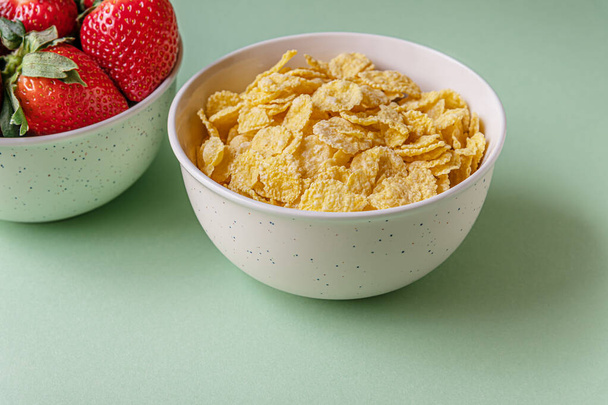 cornflakes and ripe juicy strawberries in bowls on a light green surface - Photo, Image
