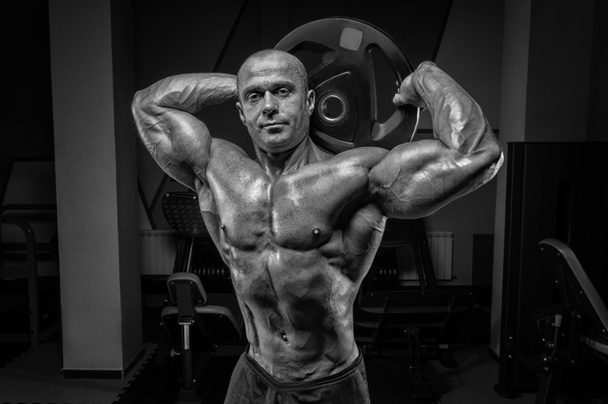 Homme musclé posant dans la salle de gym avec un disque d'haltère. Concept de bodybuilding et powerlifting. Techniques mixtes - Photo, image
