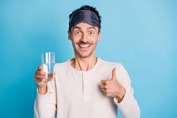 Photo portrait of man holding water glass in one hand showing thumb up isolated on vivid blue colored background - Фото, изображение