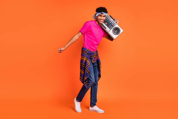 Full size photo of dark skin happy man hold boombox on shoulder wear tight shirt isolated on orange color background - Foto, Imagen