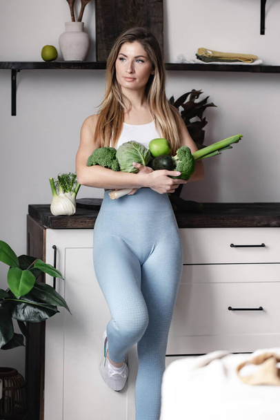 A fitness woman holds a full of fresh raw green vegetables- fennel, broccoli, avocado, apple, leek, cabbage. Healthy detox vegan dieting food. - Фото, изображение
