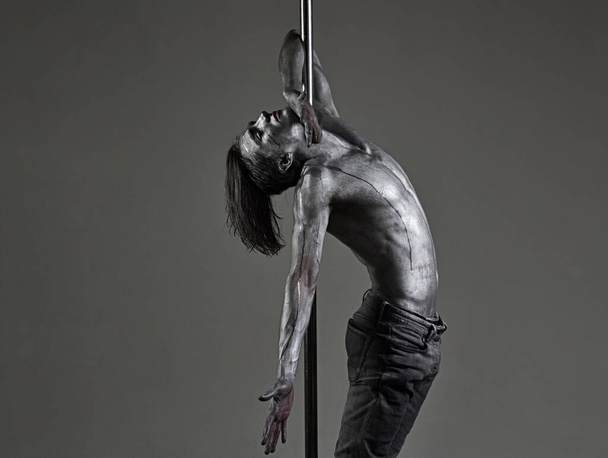 Pole dancer man with bare naked body torso. Pole dancing guy makes figure on pole. Guy hanging on metallis pole. - Fotoğraf, Görsel